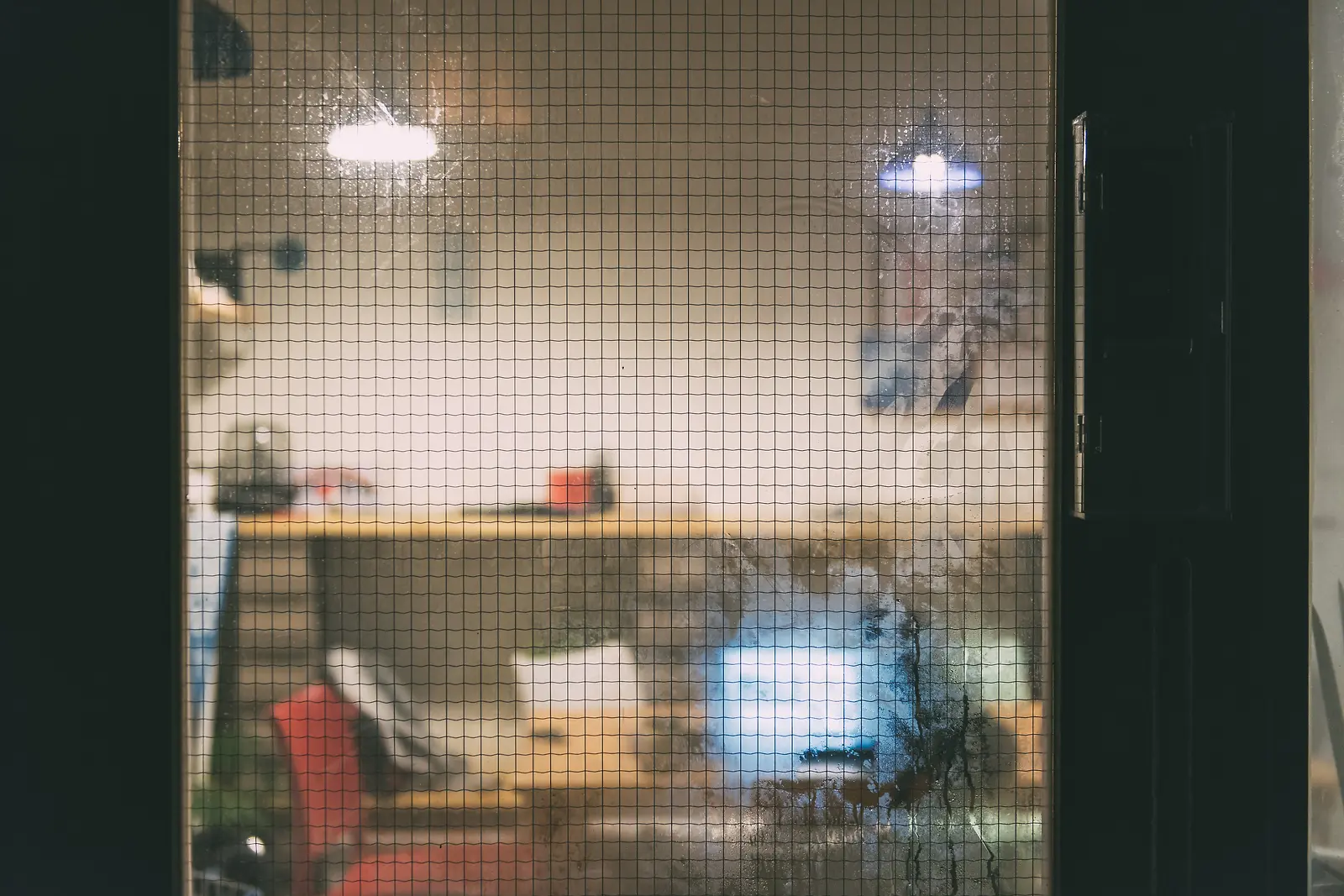 망이 있는 창 너머로 보이는 실내 조명과 탁자