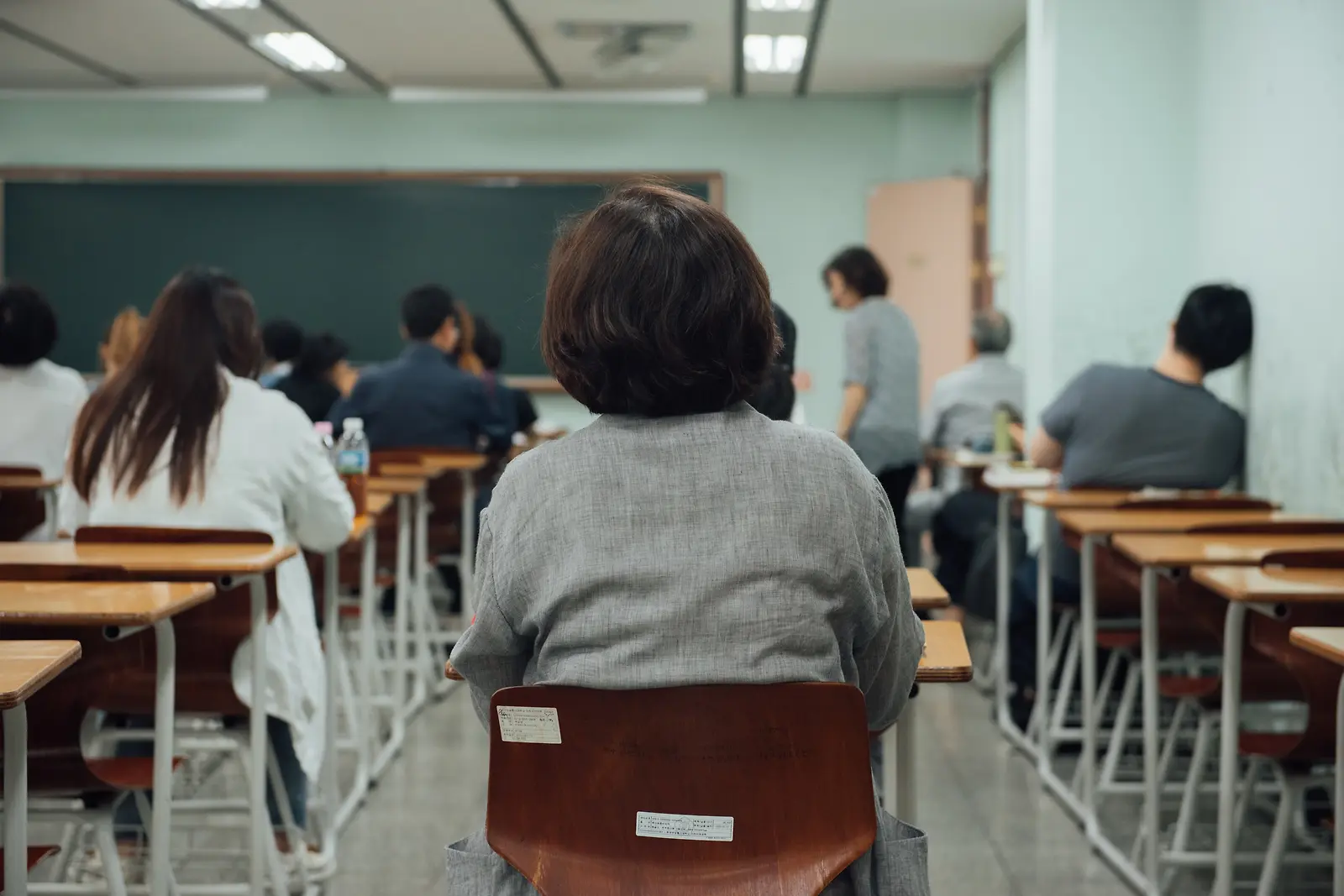 교실 책상에 앉아 수업을 듣는 어머니와 학생들의 뒷모습