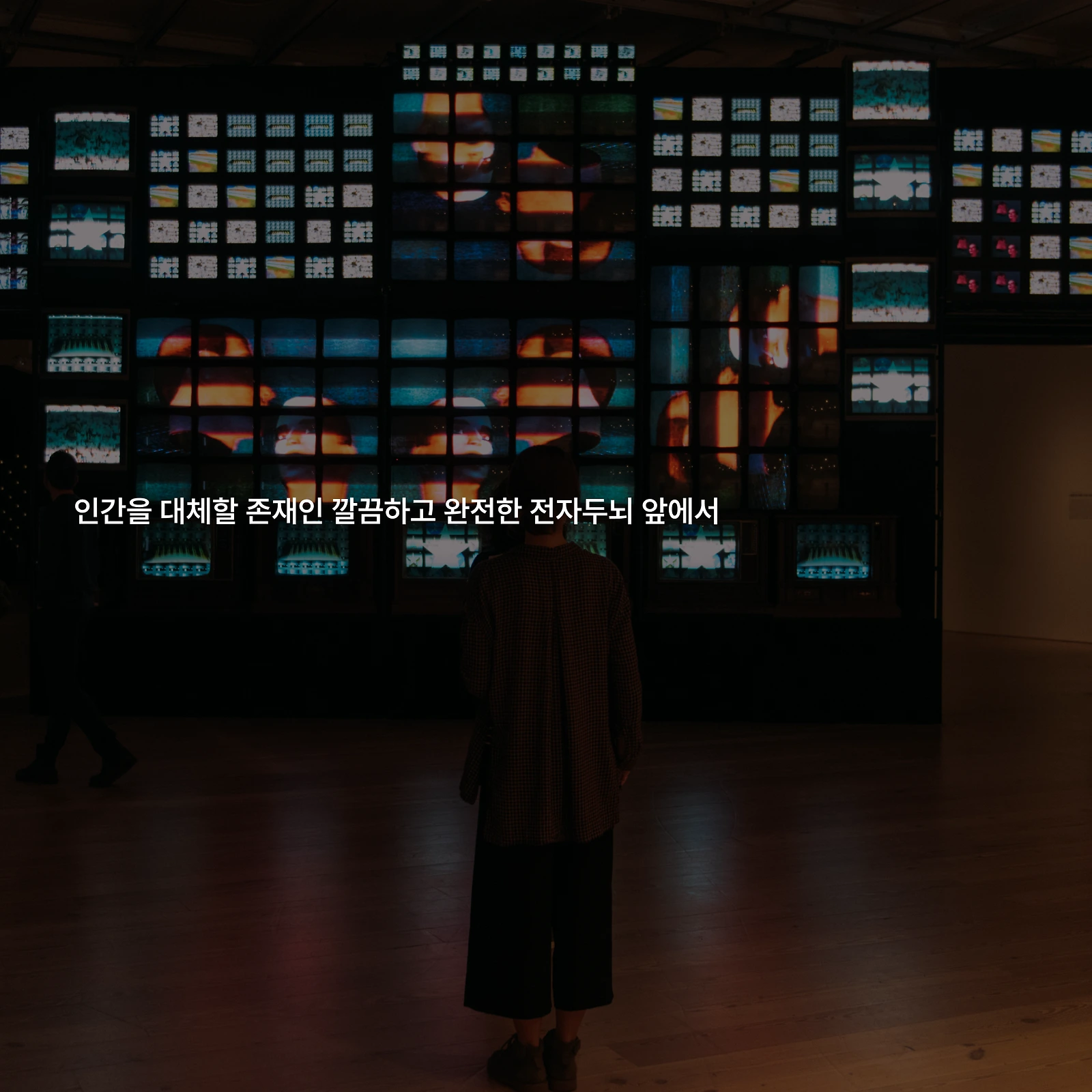 여러 화면이 설치된 전시장과 그 앞에 서 있는 관람객