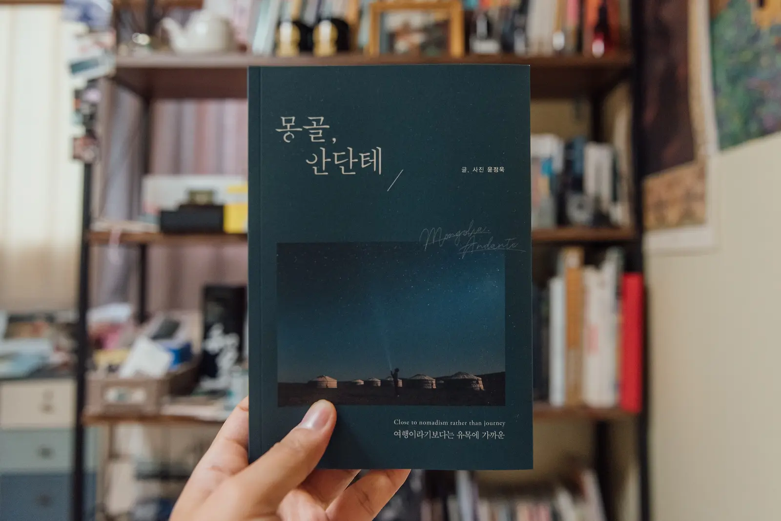 책장 앞에서 손에 들어 보인 몽골, 안단테 책 표지